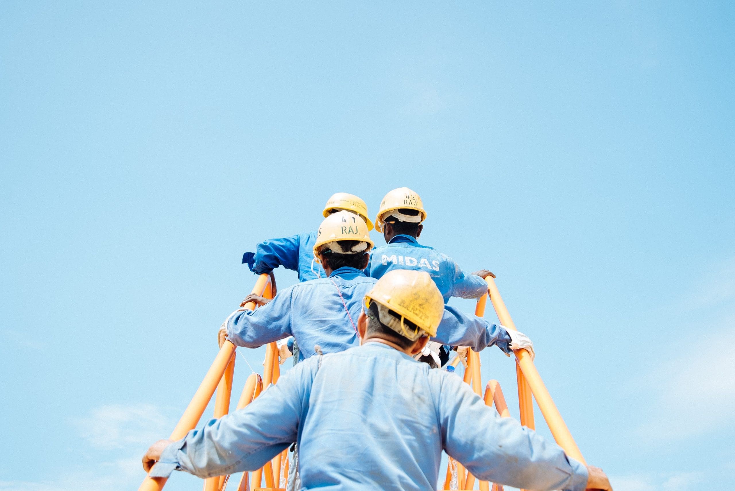 construction workers in hard hat climbing up stairs with blue sky in background